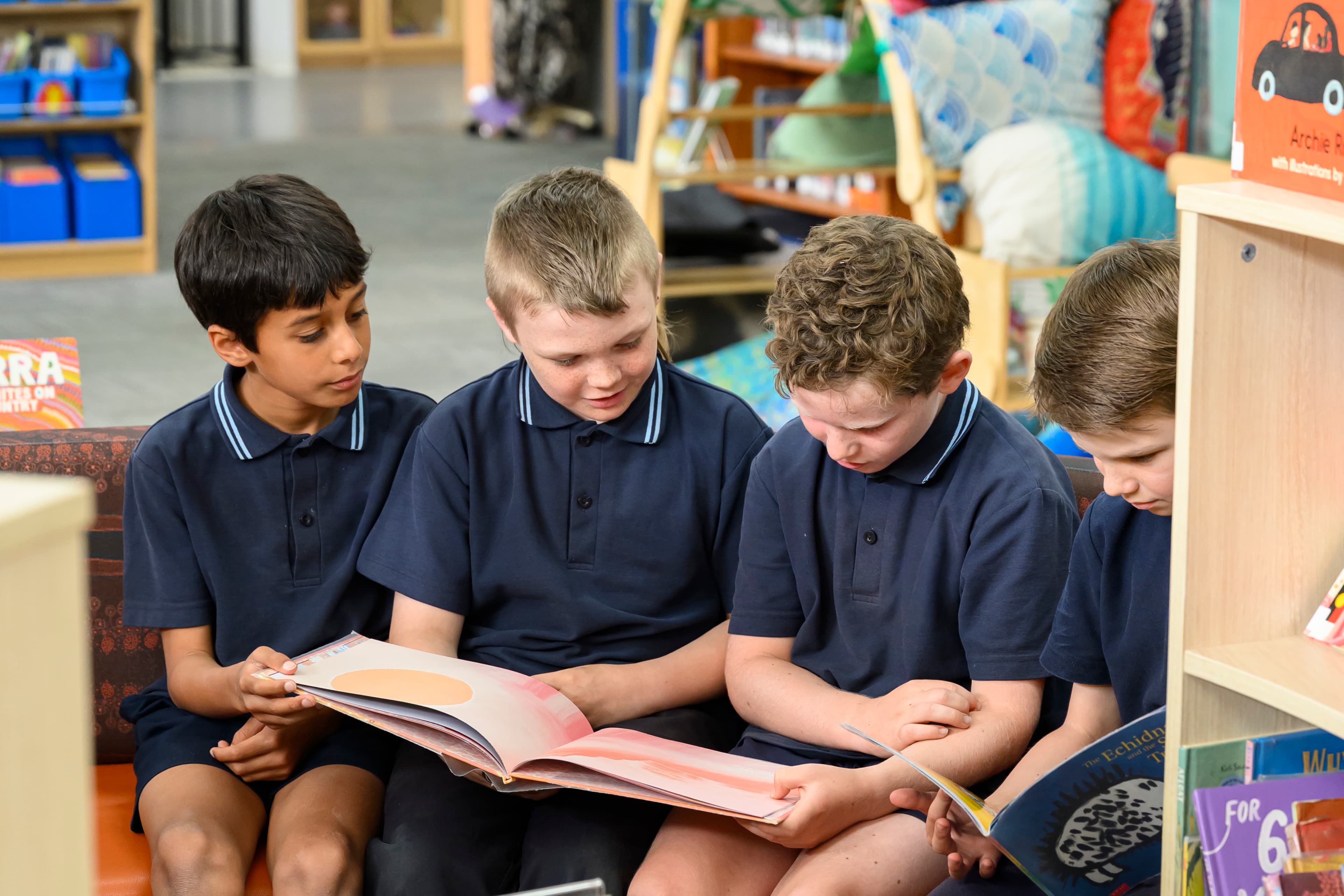 Four boys in navy shirts reading a book