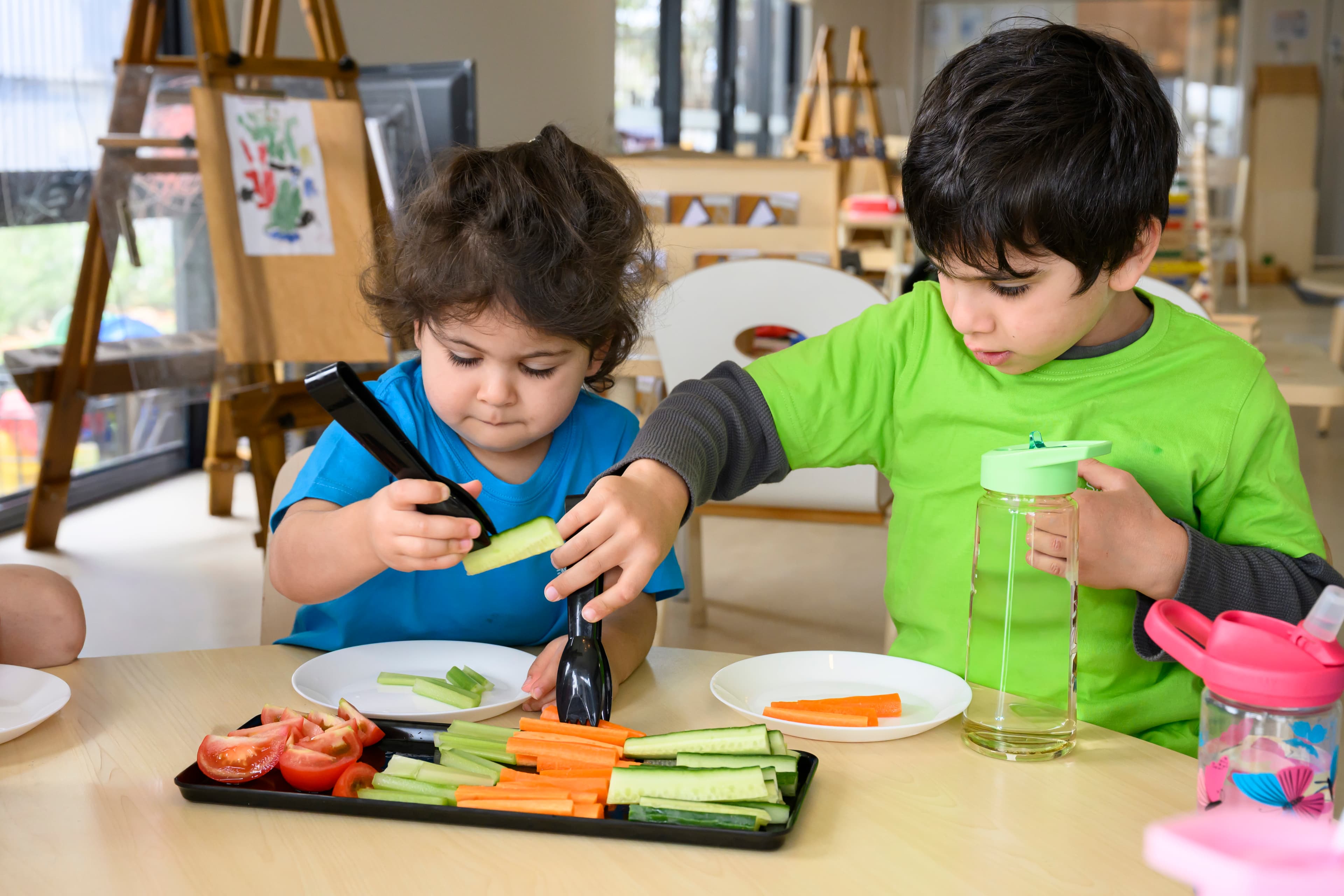 a boy and a girl having carrots and cucumber at an early childhood service