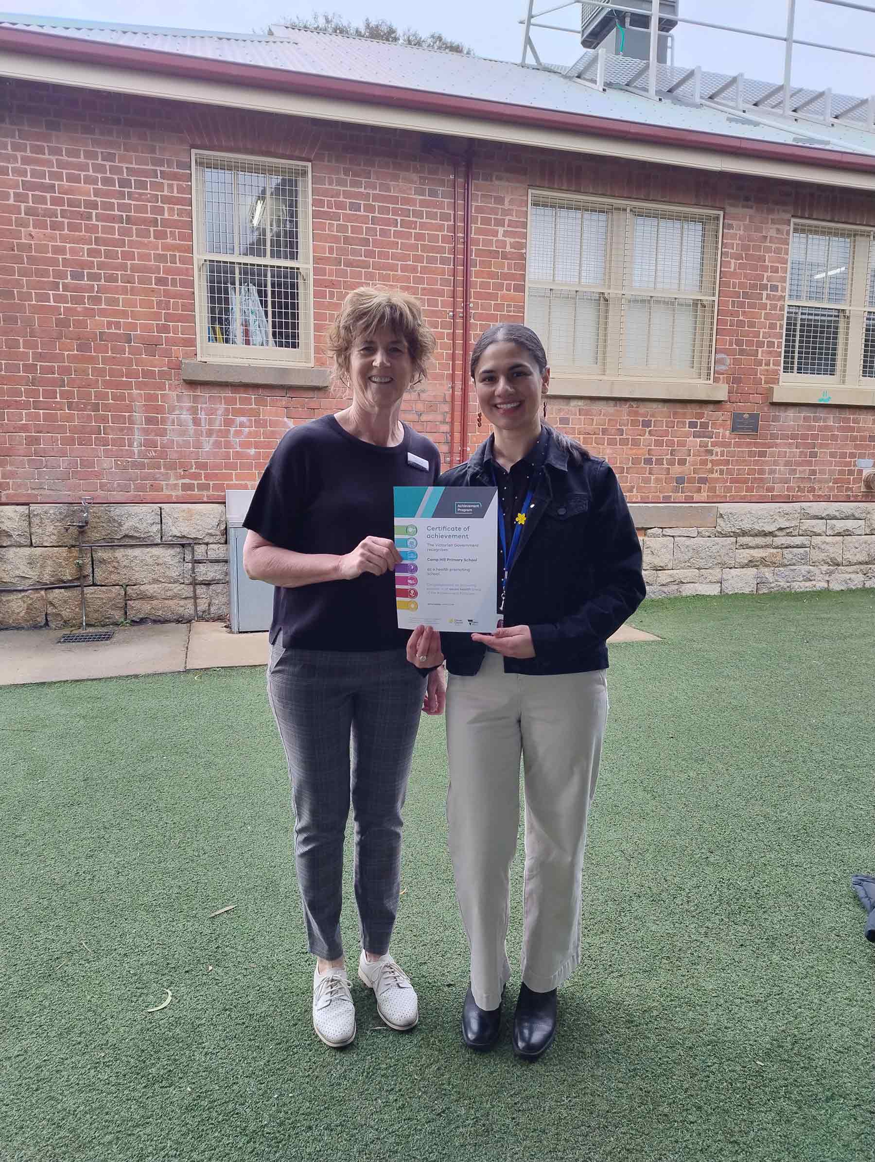 Two women dressed in black smiling and displaying a certificate