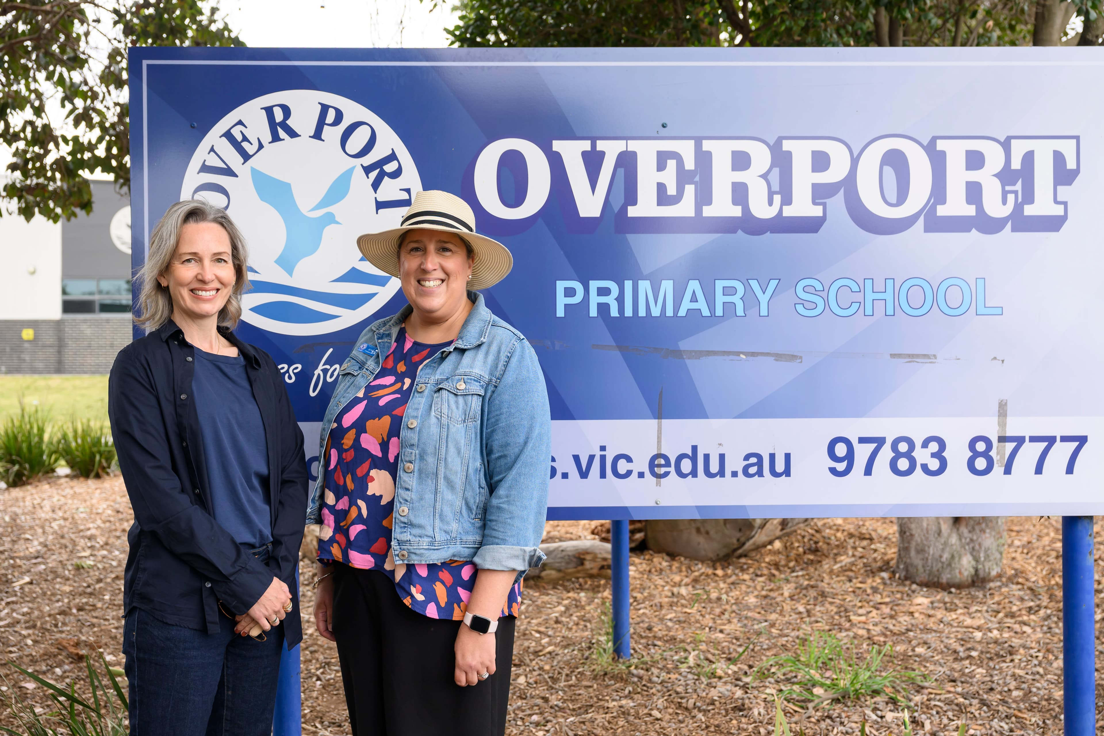 Two women smiling outdoors with a sign in the background