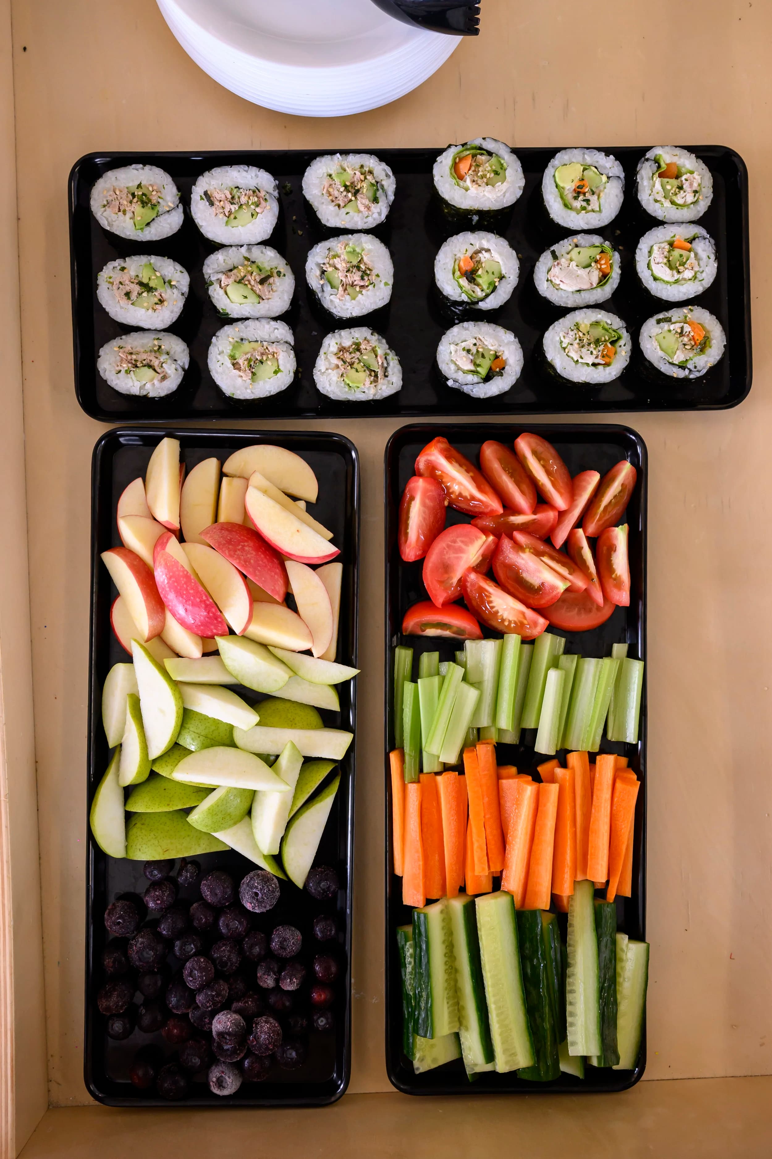 three platters of sushi, fruit and vegetable displayed on a table